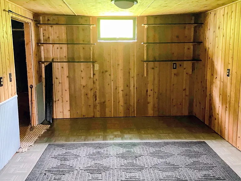 Massive basement bedroom with wood plank walls and ceiling. Window has been replaced with larger egress window that opens easily for air flow.