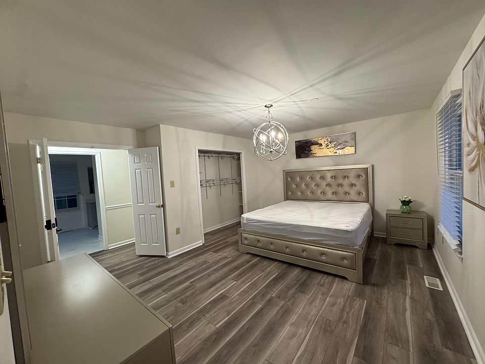 Spacious bedroom with a tufted bed, large closet system, and easy-care flooring, plus a window with blinds for light control.