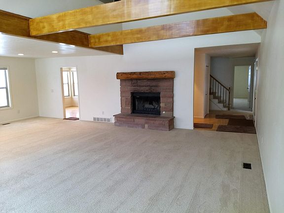 Carpeted living room with vaulted ceiling. Front entry door to right with oak wood flooring.