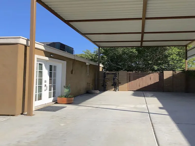 Detached casita exterior at, Tempe rental home. Features a private entrance with white French doors, a spacious covered carport, concrete driveway, and a gated side yard entrance. Perfect guest house layout for a top Tempe, AZ vacation stay.