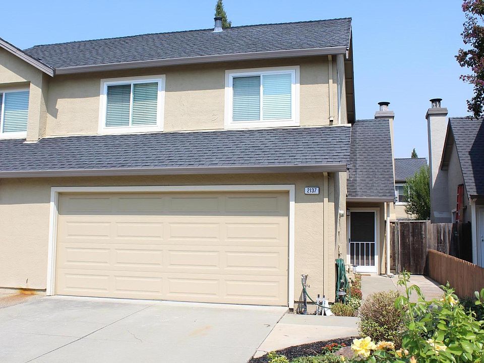 Front view of townhome with lush garden out front featuring drought resistant flowers, roses, begonias, mulch and rock features.
