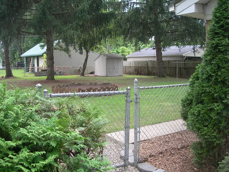 Fenced back yard with storage shed. Small raised garden soil.