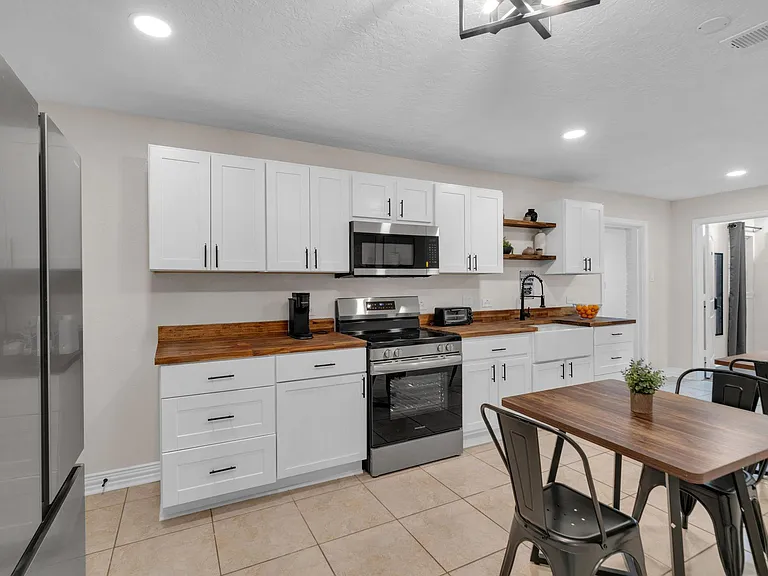 Spacious kitchen with ample white cabinetry, butcher-block counters, and stainless steel range, microwave, and fridge.
