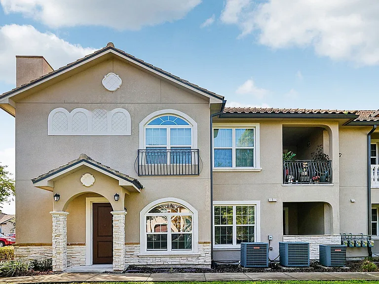 Charming two-story apartment building with elegant balconies and stone accents, set against a bright blue sky.