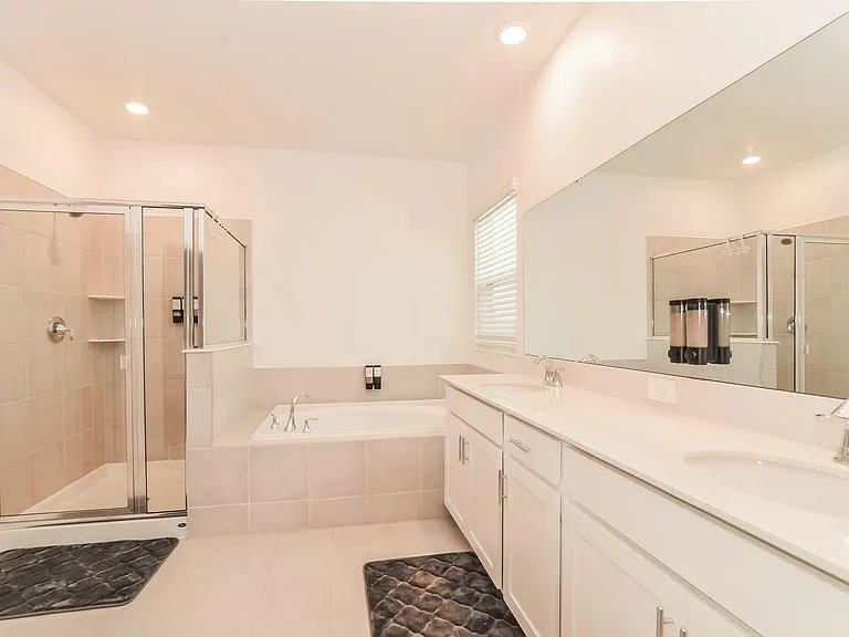 Spacious bathroom with dual-sink vanity, oversized mirror, soaking tub, and separate glass-enclosed shower.