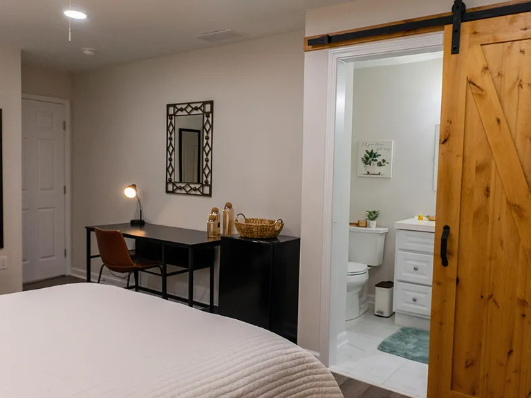 Private bedroom with a dedicated desk, mini fridge and easy access to a bathroom, featuring a sliding barn-style door.
