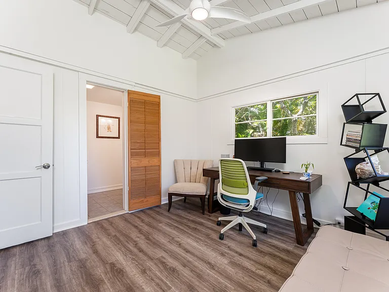 Bedroom 3 with vaulted ceilings, abundant natural light, and an ensuite bathroom. Currently staged as a home office with views overlooking the landscaped yard.