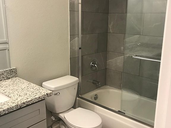 Bathroom with extra storage cabinets for towels and linens, porcelain tile inside shower and sliding glass shower door.