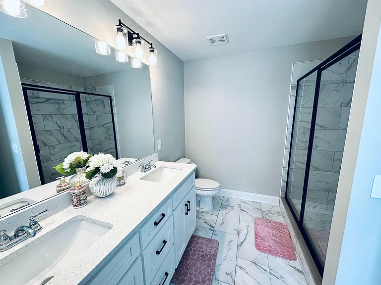 Spacious bathroom with dual-sink vanity, ample counter space, and a glass-enclosed shower with tile surround.