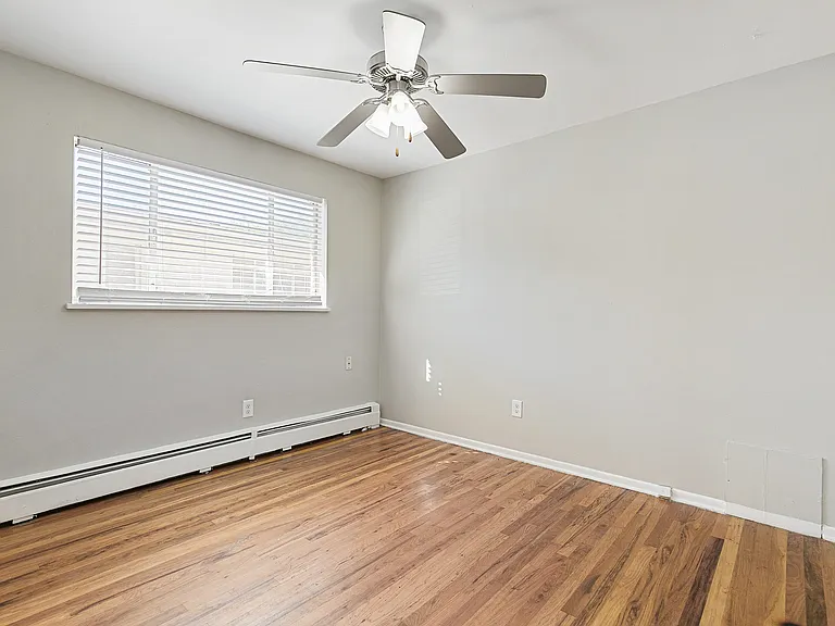 Bright bedroom with sleek wooden floors, modern ceiling fan, and large window providing ample natural light.