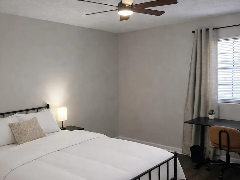 Furnished bedroom with a full bed, ceiling fan with light, and a dedicated desk area by the window with curtains.