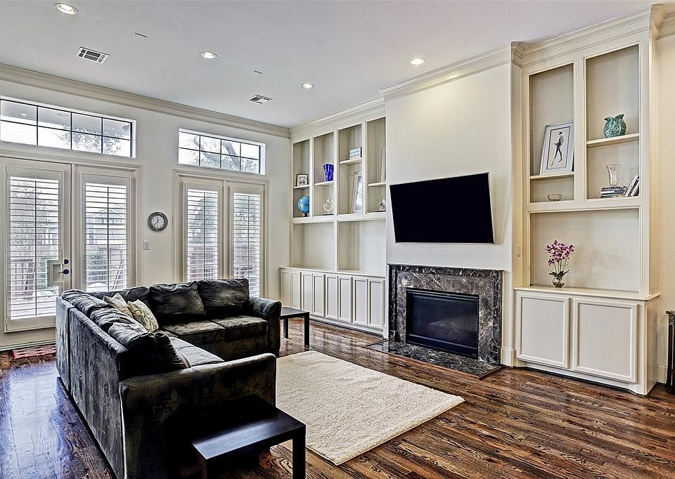 Desirable first floor living room is bright, airy, and spacious with gleaming oak floors, high ceiling with decorative crown moulding, recessed lighting, and custom built-in bookcases flanking a granite tiled gas-log fireplace. French doors lead to t
