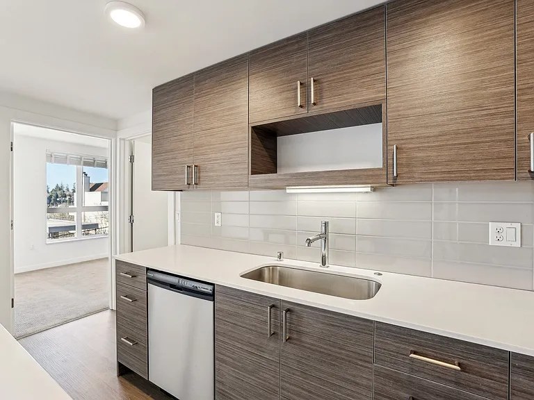 Sleek modern kitchen at 4400 Alaska in Seattle, WA, featuring contemporary wood-grain cabinetry, pristine white countertops, stainless steel sink, and conven...