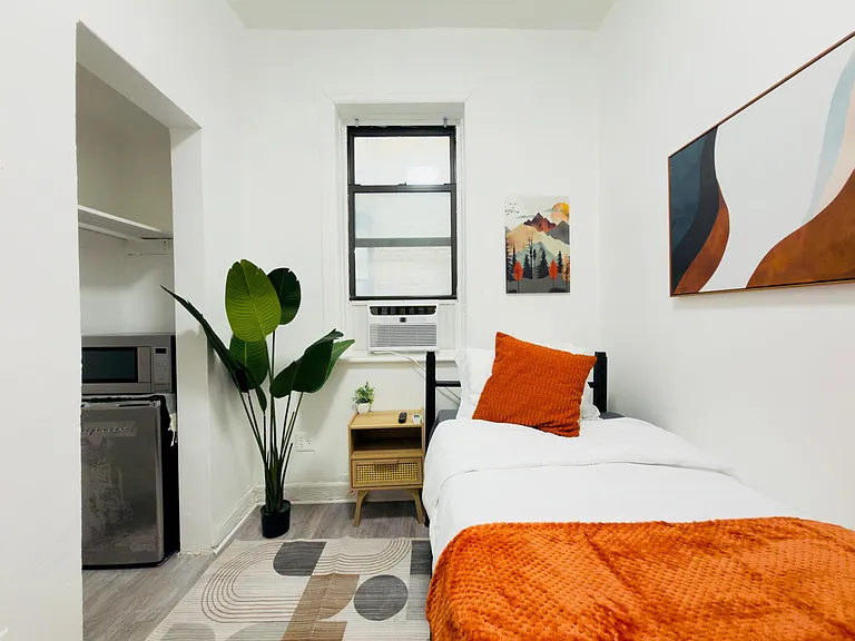 Furnished bedroom with a bed, nightstand, and window A/C, plus convenient built-in nook storage and wall art.