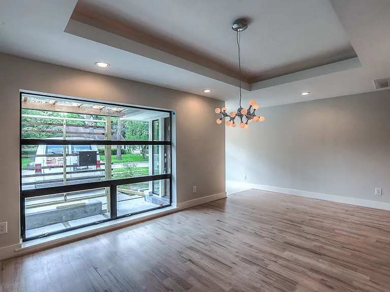 Front dining room with tray ceiling, designer bubble chandelier, oversized picture window with pergola view, and new hardwood floors installed during renovation.