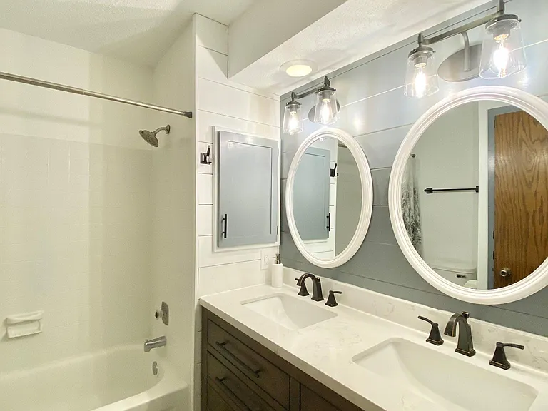 Newly remodeled full bathroom with gray oak vanity, carrara white stone vanity top, and integrated double white sinks.