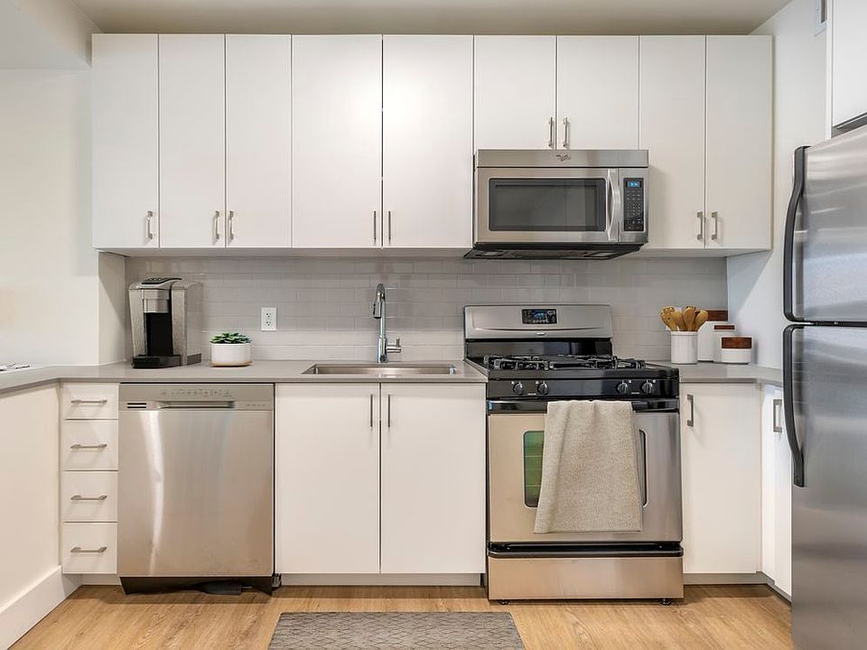 Renovated II North/South kitchen with stainless steel appliances, grey quartz countertops, white lacquer cabinetry, white tile backsplash, and hard surface flooring