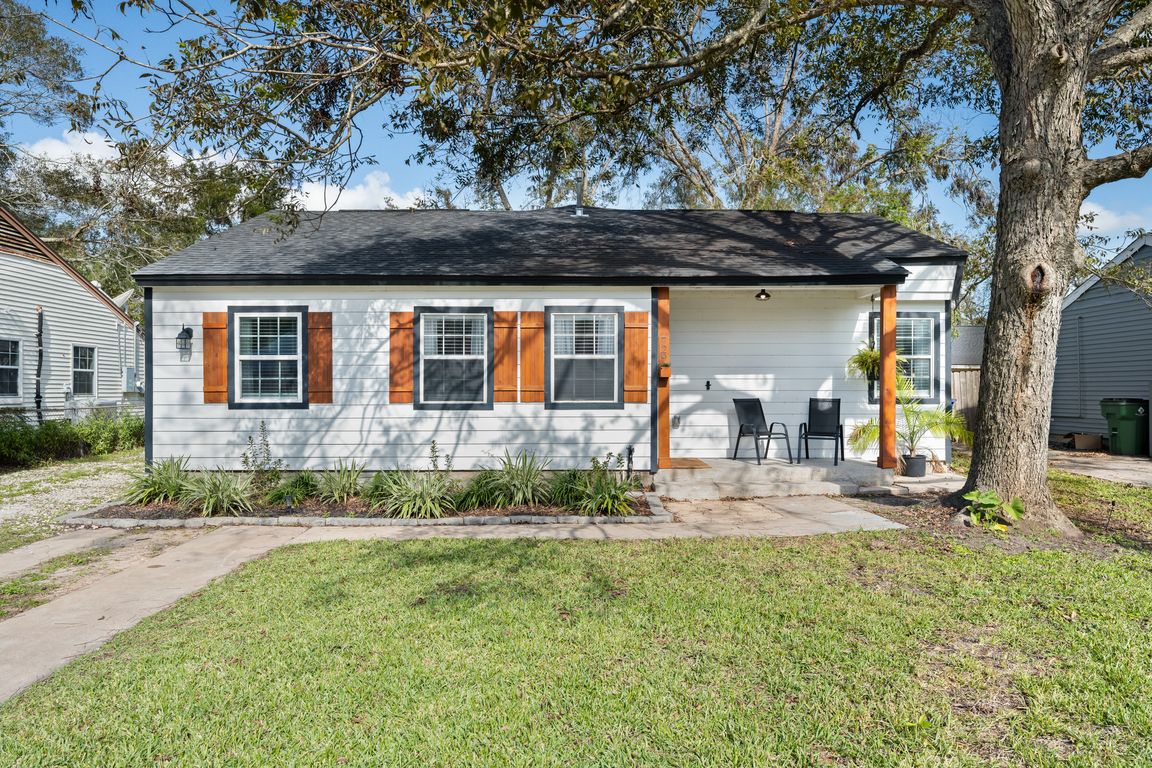 Charming single-story home featuring fresh white siding accented by natural wood shutters and trim. Mature trees and simple landscaping create inviting curb appeal with a welcoming walkway leading to the covered front porch.