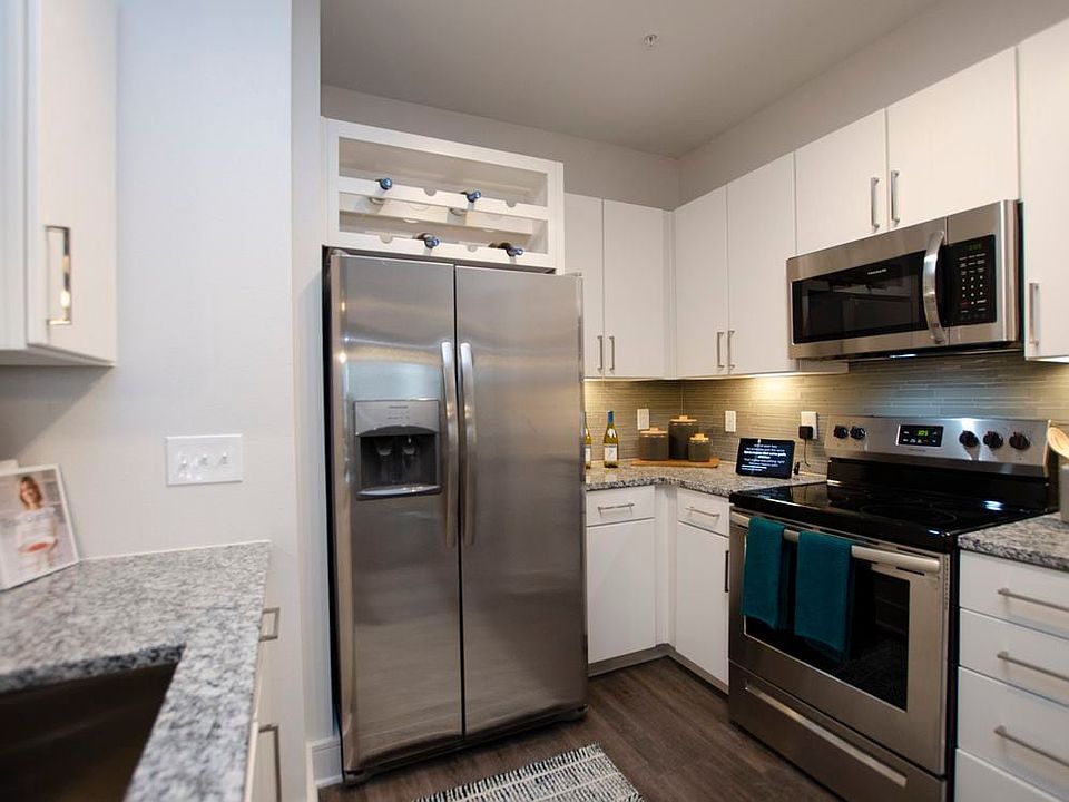 Kitchen with white cabinetry, speckled granite countertops, grey tile backsplash, stainless steel appliances, and hard surface flooring