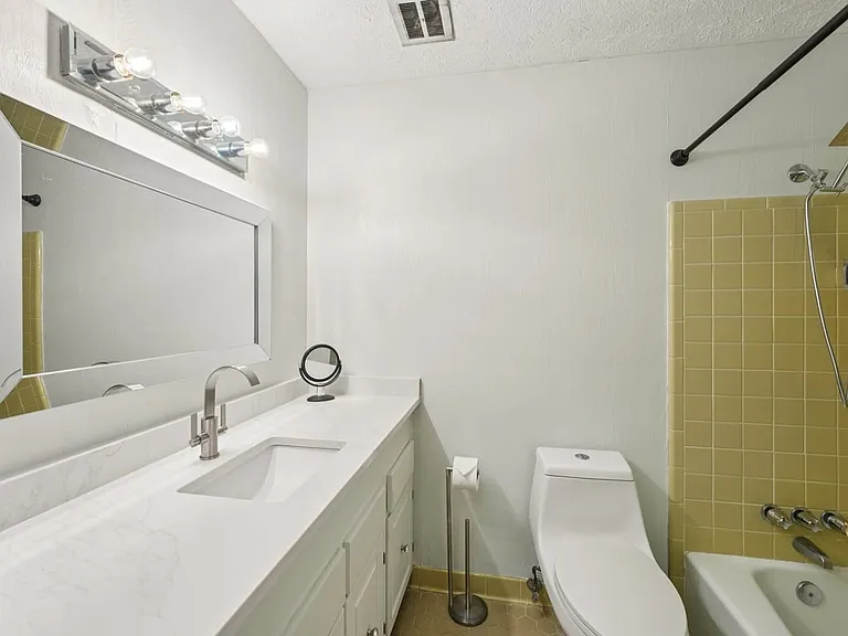 A clean and polished bathroom where bright vanity lighting, crisp white finishes, and vintage golden tile create a charming blend of function and nostalgic character.