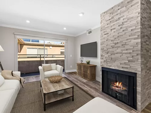 Living room with stone accented fireplace and balcony access. - Catalina Apartments
