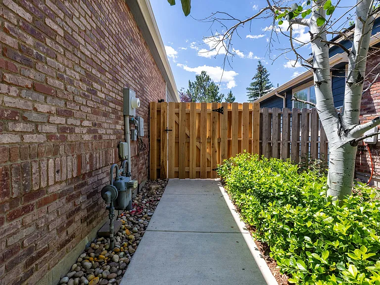 A new concrete walkway and cedar privacy gate create a clean, polished side entrance while keeping trash and recycling bins discreetly out of view.