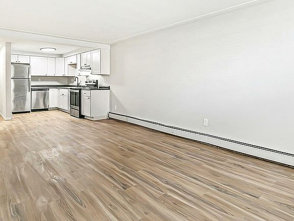 Bright, spacious open-concept apartment with sleek hardwood floors and a modern kitchen featuring stainless steel appliances and elegant white cabinetry.