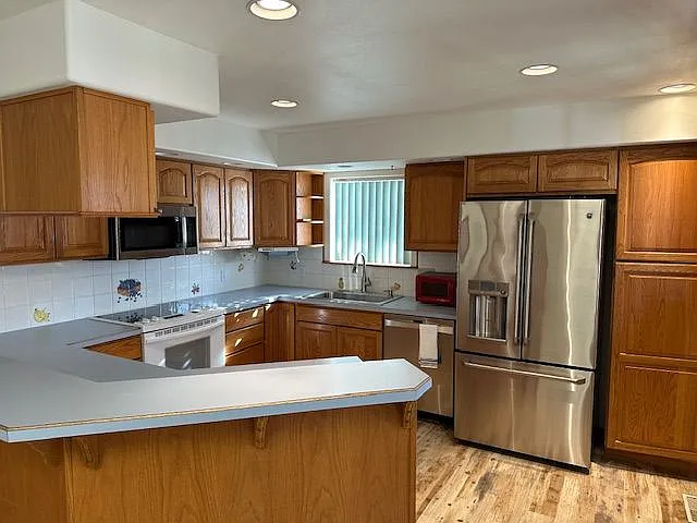 Spacious kitchen with ample cabinet space, stainless steel refrigerator, dishwasher, microwave, and recessed lighting.