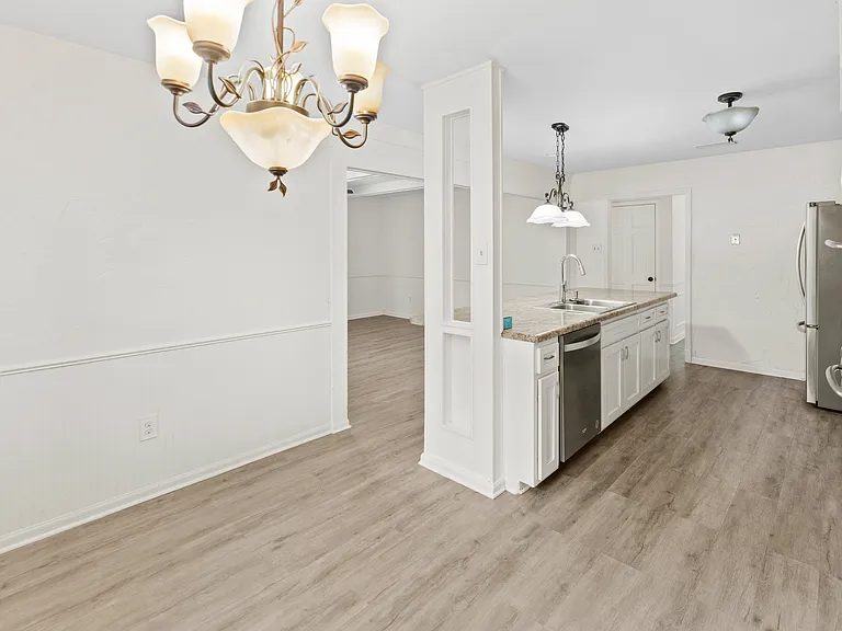 Stunning open-plan dining and kitchen area with elegant chandelier, hardwood floors, and beautiful sightlines throughout.