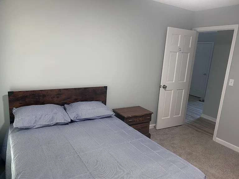 Furnished bedroom featuring a full-size bed, nightstand, and soft carpet flooring with easy access to the hallway.