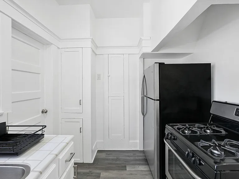 Galley-style kitchen with full-size gas range, stainless refrigerator, and tiled counters with extra cabinet storage.