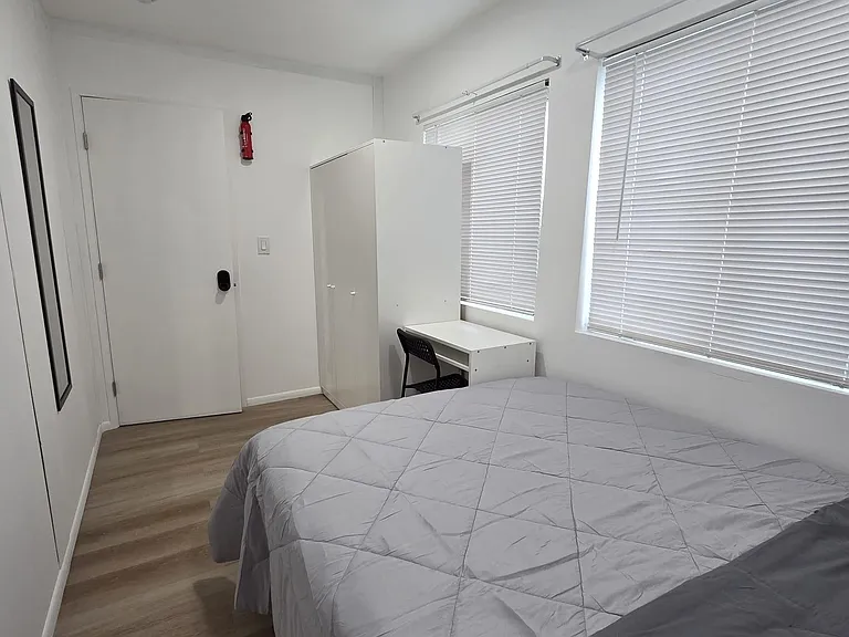 Private bedroom with wide windows and blinds, plus a dedicated desk area and wardrobe storage for everyday convenience.