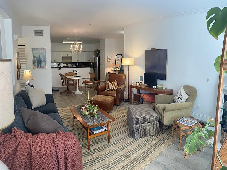 Looking back toward the kitchen from next to the balcony door. Included in living room: 2 chairs and recliners, arched shelving, couch, coffee and console tables, rug, 2 side tables next to couch, and 3 lamps.