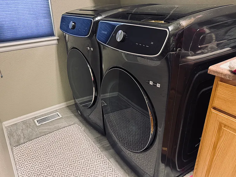 Shared laundry area with washer and dryer located on the main level near the stairs to the basement apartment.