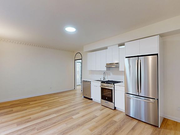 Kitchen featuring stainless steel appliances, cabinetry, and warm wood flooring, illuminated by natural light