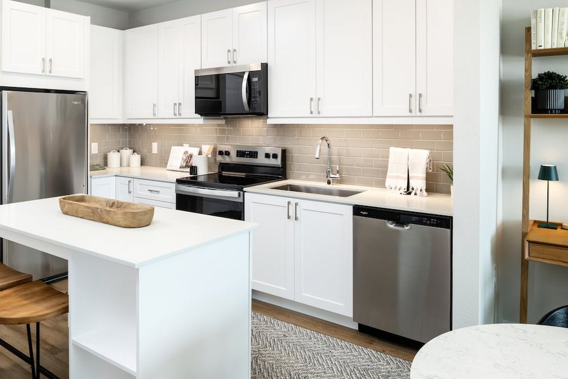Finish Package I kitchen with stainless steel appliances, white cabinetry, grey tile backsplash, white quartz countertops, and hard surface flooring
