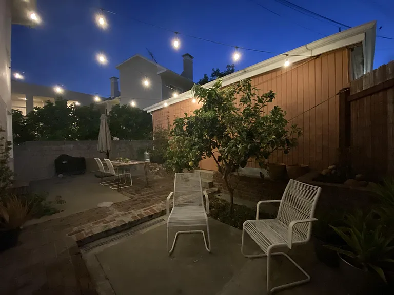 Another angle of the patio with huge shade canopy, edison string lights, an exterior power plug so you can sit outside and work on your computer, tons of plants, and a pink lemonade lemon tree! Night shot.