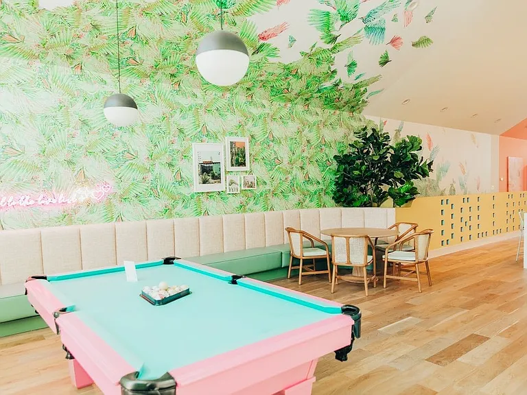 Recreational room featuring a pastel-colored billiards table, upholstered banquette seating, wood-finish flooring, and tropical-themed wall decor