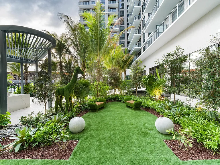 A sculptural garden courtyard at Modera Aventura, where tropical landscaping, playful art, and shaded seating create a distinctive outdoor retreat.