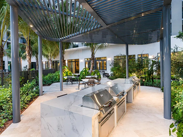 Outdoor kitchen design framed by a slatted canopy, marble prep surfaces, and layered tropical landscaping for effortless open-air gatherings in Miami.