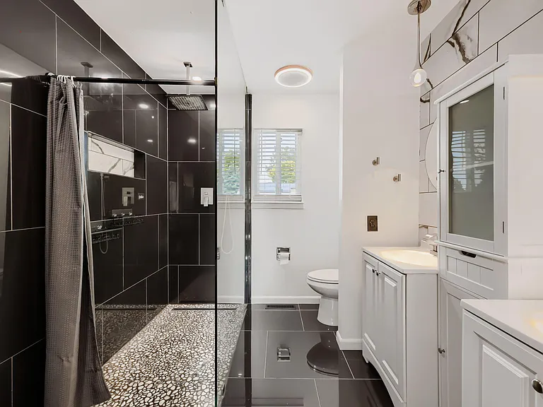 Updated bathroom with dual-sink vanity, ample storage, and a tiled shower, plus a window for natural light.