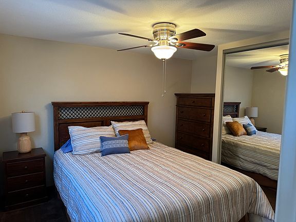 Master bedroom with queen size bed, ceiling fan, tall boy dresser, night stand and mirrored closet doors.