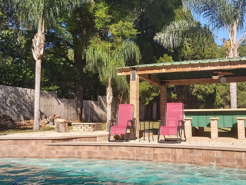 Large in-ground pool with fountain water features, plenty of lounging chairs, covered bar eating area, BBQ, and firepit area.
