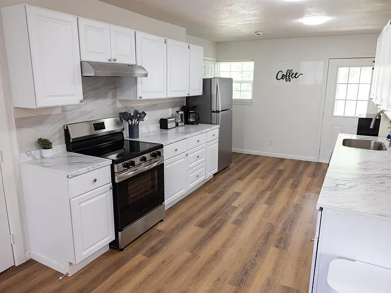 Updated galley kitchen with ample white cabinetry, stone-look counters, and stainless appliances, plus a convenient exterior