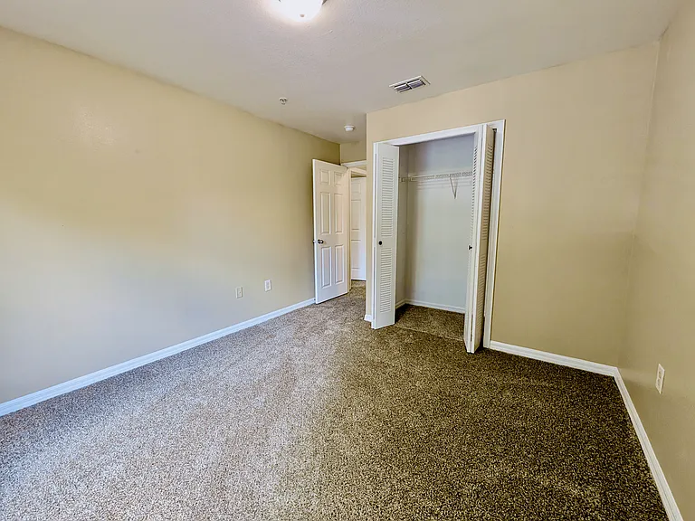 Bright and airy bedroom with plush carpet and open closet, perfect for a cozy and functional living space.