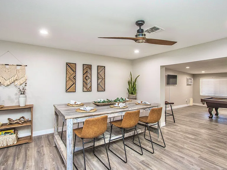 Charming dining area at Casa Del Sol, Tempe rental home. Features a rustic wooden table, chic leather chairs, boho decor, and an open layout leading to a game room with a pool table. Perfect for group gatherings in a top Tempe, AZ vacation spot.
