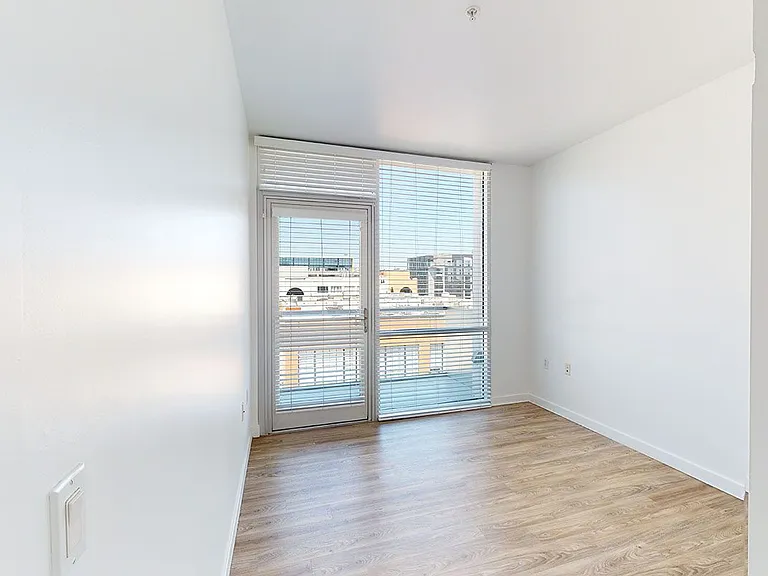 Spacious apartment bedroom with wood-style flooring and floor-to-ceiling windows.