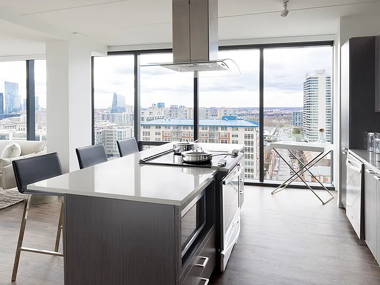 Large kitchen island with sleek gas cooktop looking into living surrounded by floor to ceiling windows