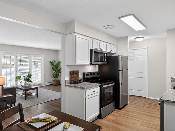 Contemporary open-plan kitchen and living room with sleek stainless steel appliances, granite countertops, and elegant hardwood flooring, complemented by natural light from large windows and stylish decor.