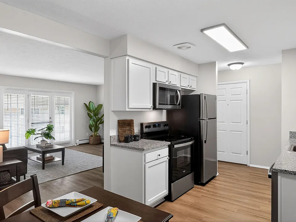 Contemporary open-plan kitchen and living room with sleek stainless steel appliances, granite countertops, and elegant hardwood flooring, complemented by natural light from large windows and stylish decor.